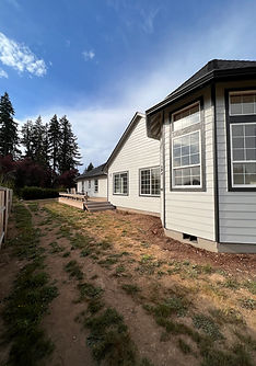 Modern white house exterior with large windows, grassy yard, and forest backdrop.